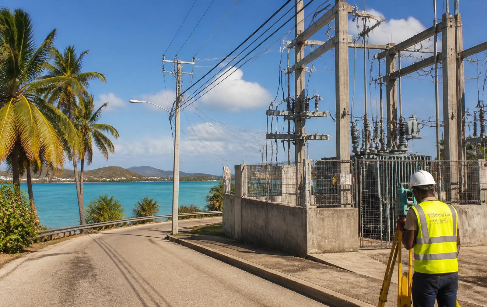 Poste de transformation HTA et lignes électriques en bord de mer, technicien avec station topographique